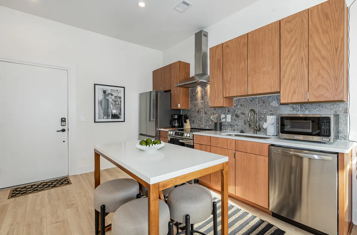 A modern kitchen scene with a spacious island, gleaming stainless steel appliances, warm wood cabinetry, and a decorative fruit bowl as a centerpiece. The setup suggests an environment equally suited to preparing quick breakfasts or hosting gatherings, with stylish finishes and thoughtful touches throughout.