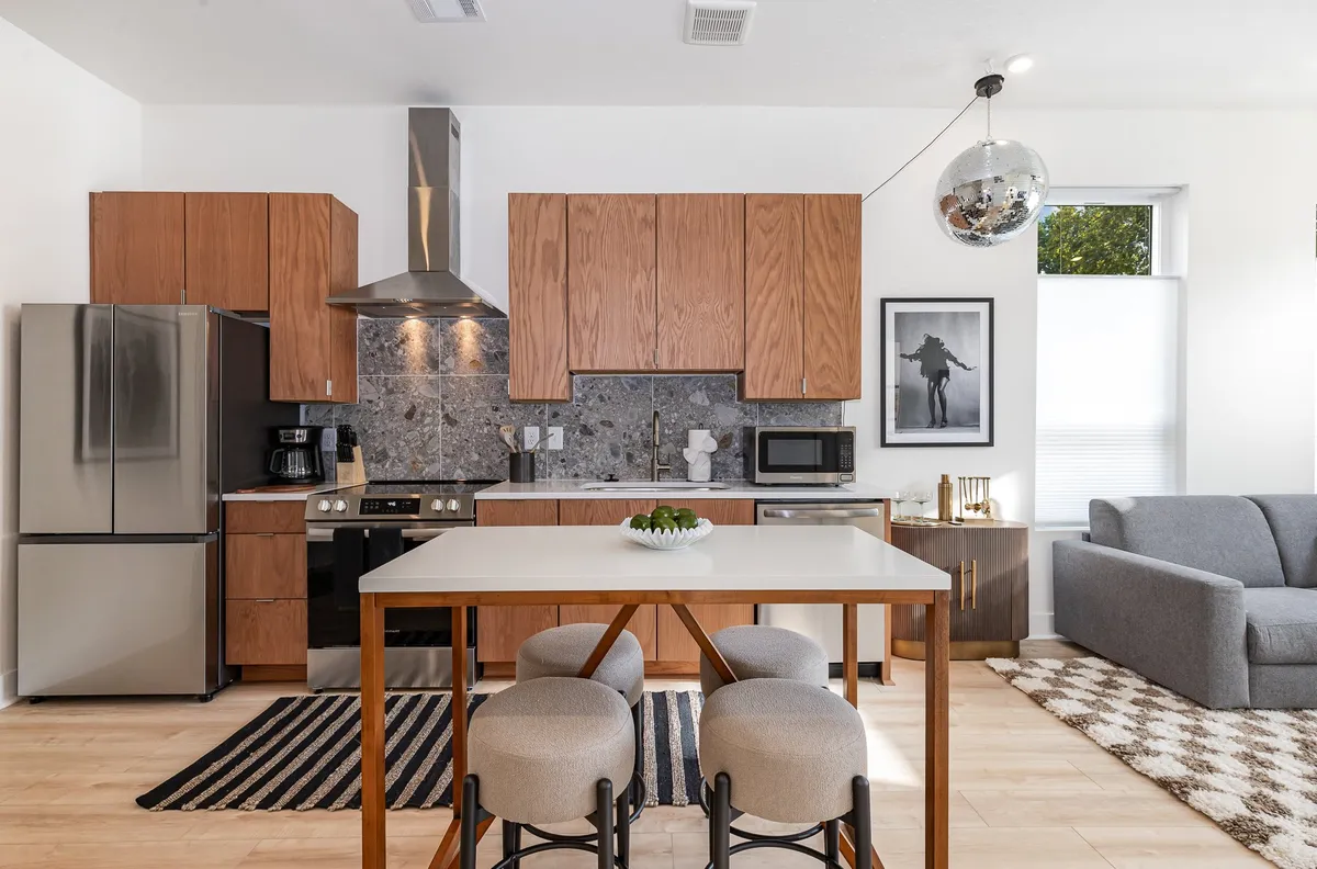 This image features a stylish, contemporary interior centering on a kitchen island, with a refrigerator, comfortable sofa, and wall artwork visible. The layout suggests an open, welcoming living space suited for cooking, dining, and relaxing, with a clear view of kitchen amenities and seating.