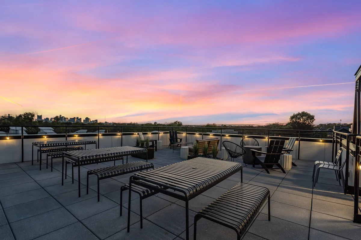 A rooftop patio with striped benches and outdoor chairs overlooks the city skyline as the sun sets, creating a peaceful and inviting atmosphere for families to unwind together after a day of adventure.
