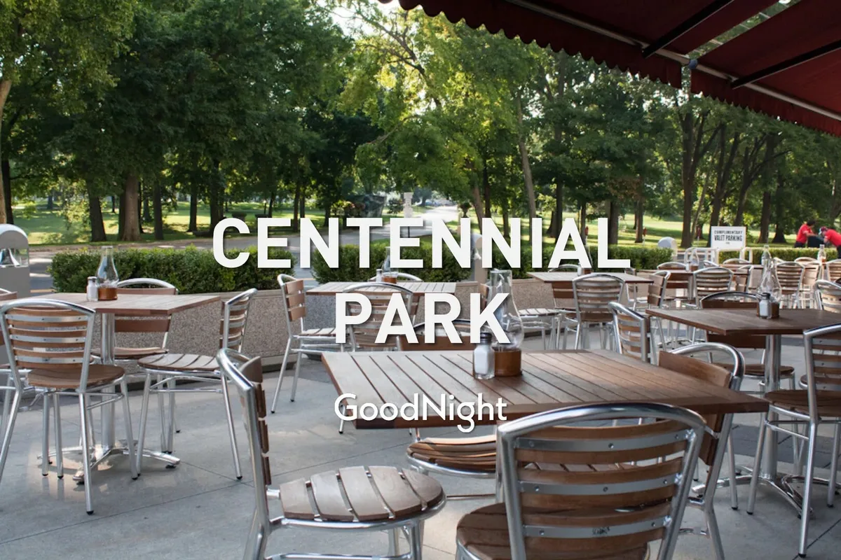 A welcoming outdoor café area with wooden tables and green trees set against a park background. The space invites socializing, dining, or people-watching—activities well-suited for pet owners looking to relax with their companions.