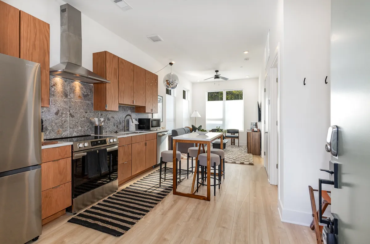 A view capturing the kitchen appliances, a dining table set for meals, and a cozy living area with seating all in one frame. The space is welcoming and contemporary, designed for socializing, dining, or simply unwinding after a long day.