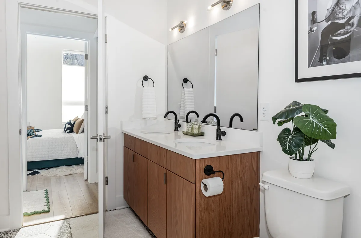 A modern bathroom with a double sink vanity, large mirror, and stylish fixtures. An indoor plant and a framed photo add touches of homey warmth, while the clean lines and ample lighting evoke a spa-like atmosphere.