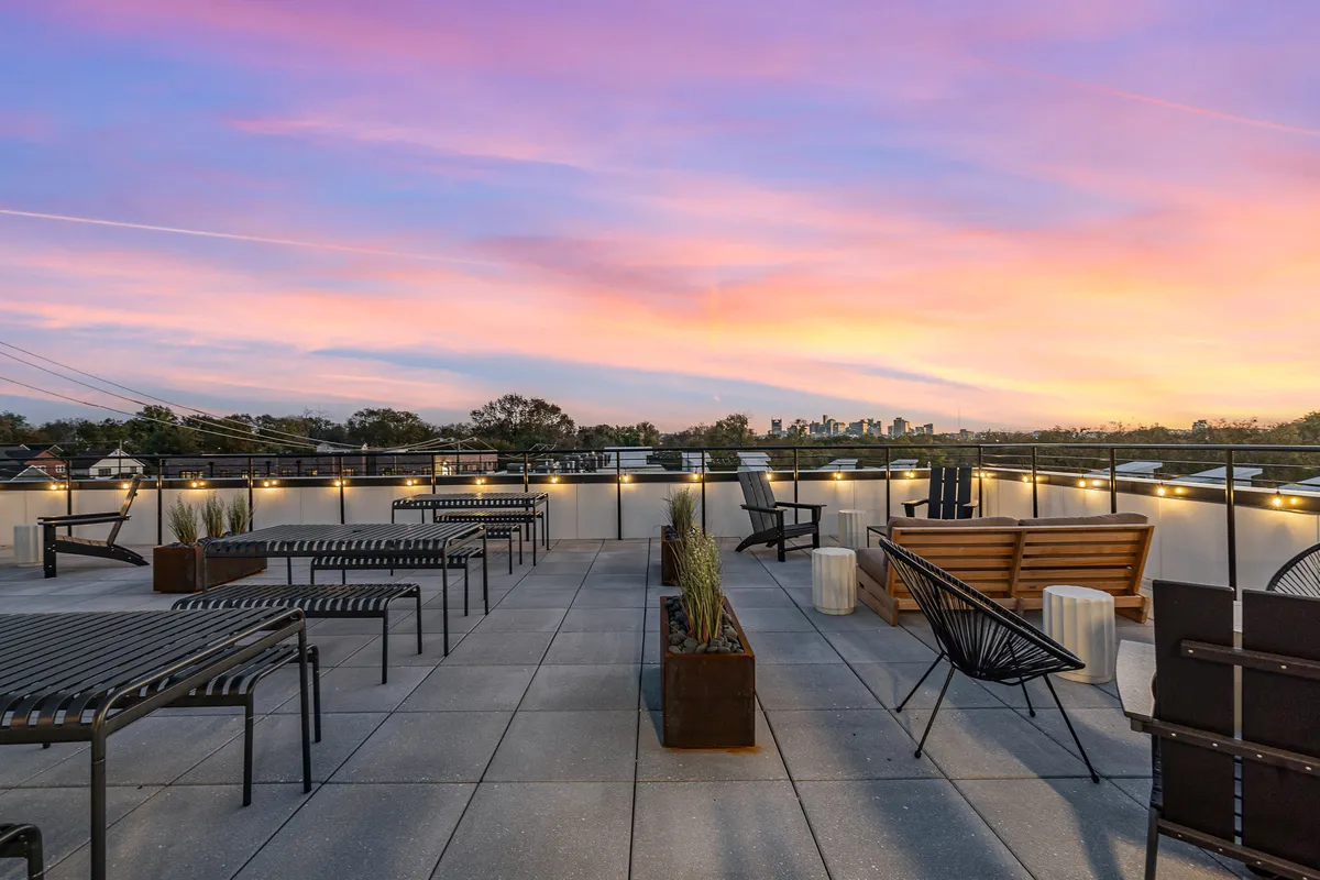 A stunning rooftop patio featuring cozy seating areas, a dining table, and panoramic views of the Nashville city skyline at sunset. The warm glow and open-air setting invite relaxation and social gatherings, embodying the spirit of al fresco dining and communal experiences.