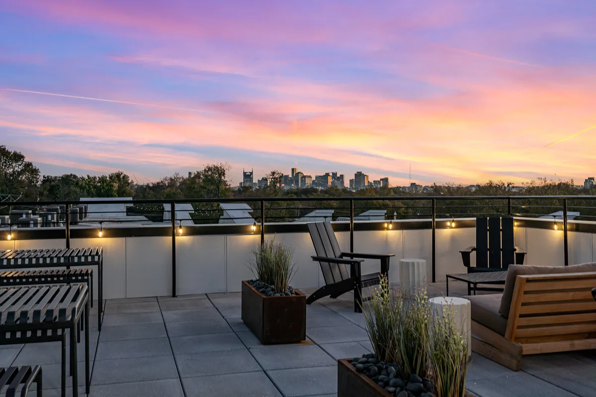 A tranquil exterior view of a rooftop patio with outdoor seating, the city skyline in the distance, and sunset colors painting the sky. This inviting communal space encourages relaxation and conversation against an urban backdrop.